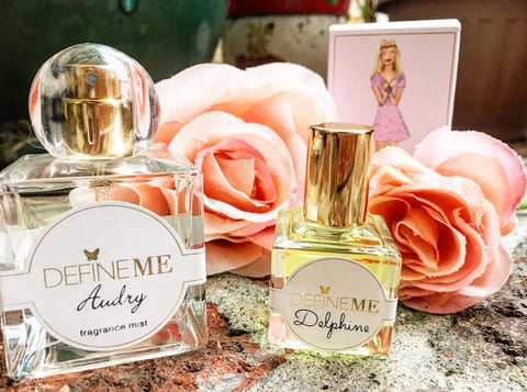 DefineMe Fragrance Mist Audry and Oil Delphine on table with pink flowers and DefineMe box in background.