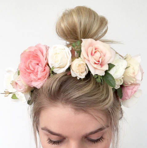 Woman with hair up wearing pink and white flower crown in her hair while looking down.