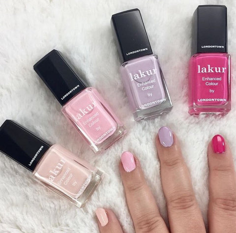 Londontown Lakur Nail Polishes lying down on a soft rug with hand in foreground with painted nails in alternating colors.