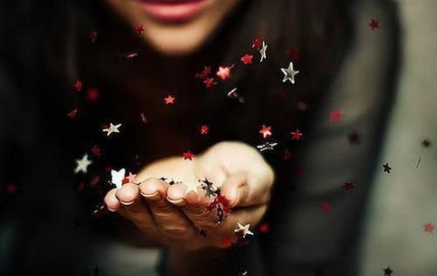 Woman holidng hand out with star confetti being blown into the air.