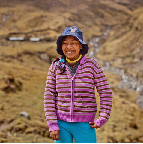 Girl in pink sweater and blue hat smiling on mountainside.