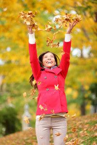 Woman in red jacket throwing up autumn leaves in the air.