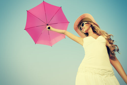 Woman in white dress and hat holding pink umbrella in the air.