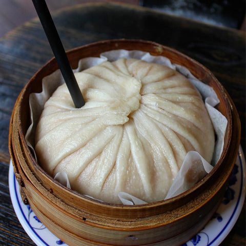 A very large soup dumpling in a steamer with a straw