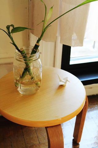 Two lucky bamboo in a mason jar and a ceramic origami crane chopstick rest, all on a bamboo stool