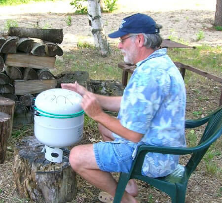 old man wearing blue button down shirt and shorts playing white medium sized steel drum