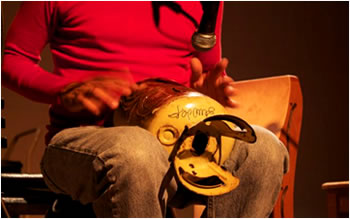 person with tongue drum instrument between his legs hands striking the drum