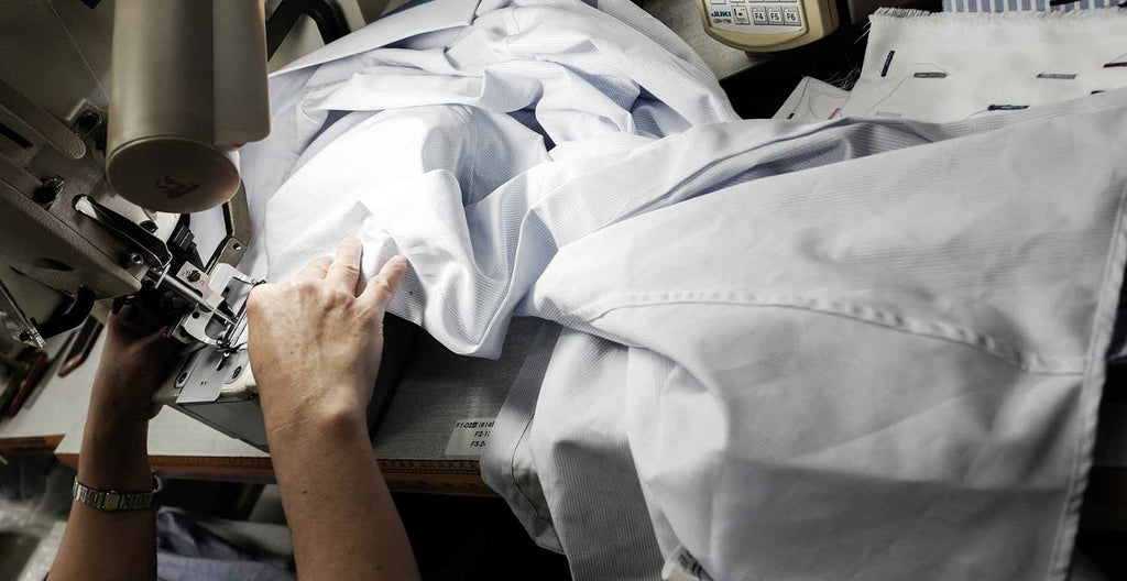 tailor in workshop stitching white custom men's dress shirt