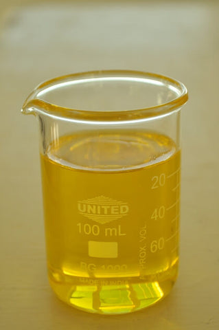 Glass beaker filled with yellow transparent jojoba oil