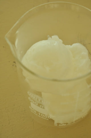 scoop of shea butter at bottom of clear glass beaker