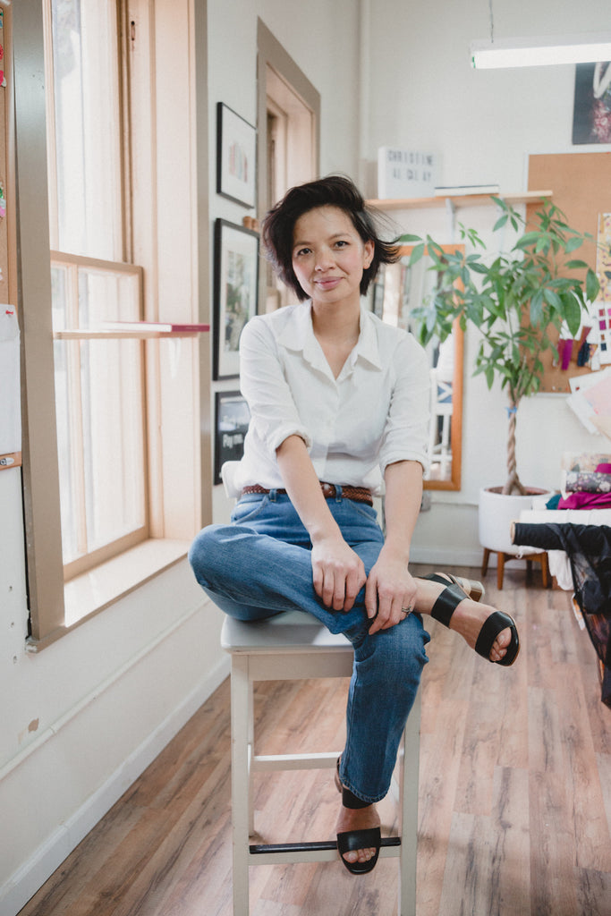 Photo of designer, Christine Alcalay sitting cross legged smiling at the camera. 