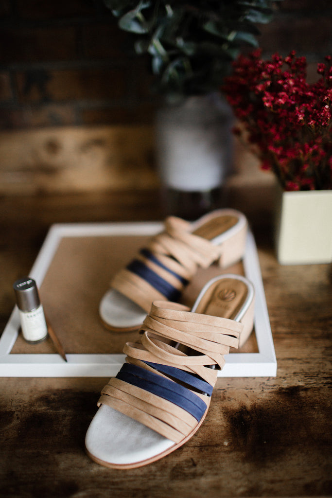 Image of the Coclico Taz Sandal placed on a wooden table with decor in background. 