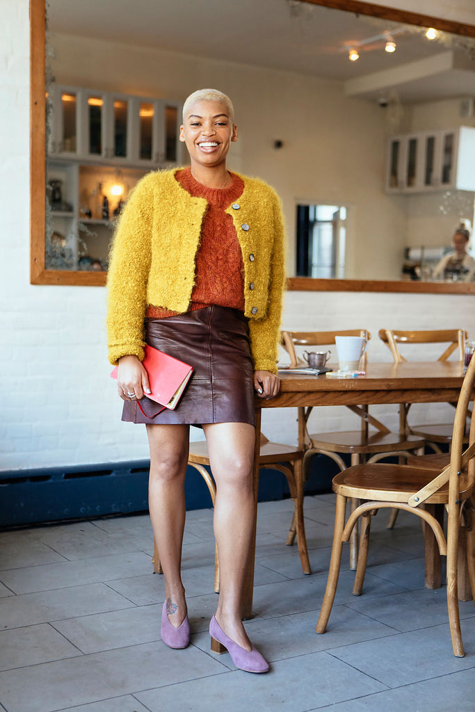 Elise Peterson, a visual artist, writer, children’s book illustrator, and on-camera host leaning on a table. 