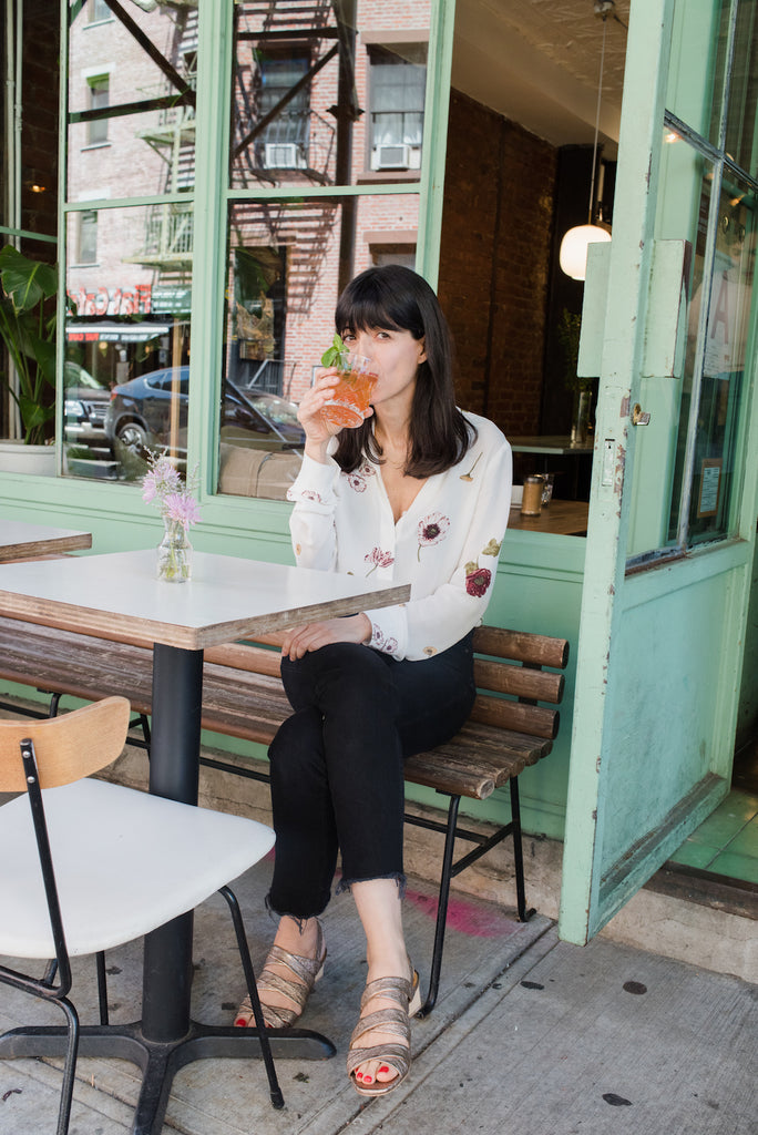 Giorgia Zedda seated outdoors on a wood bench wearing the Coclico O'Boy Sandal in Rose Metallic Leather.