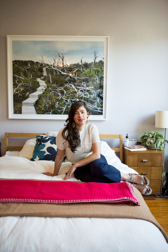 Erin Allweiss sitting to one side of the bed in her Coclico Float sandals. 