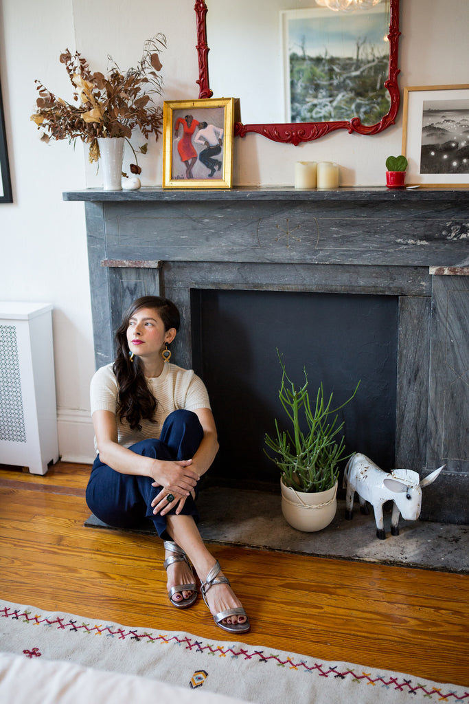 Erin Allweiss seated beside a marble fireplace in her Coclico sandals.