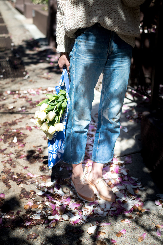 Waist-down shot of Erin Boyle holding a bag and bouquet flowers in the sunlight.