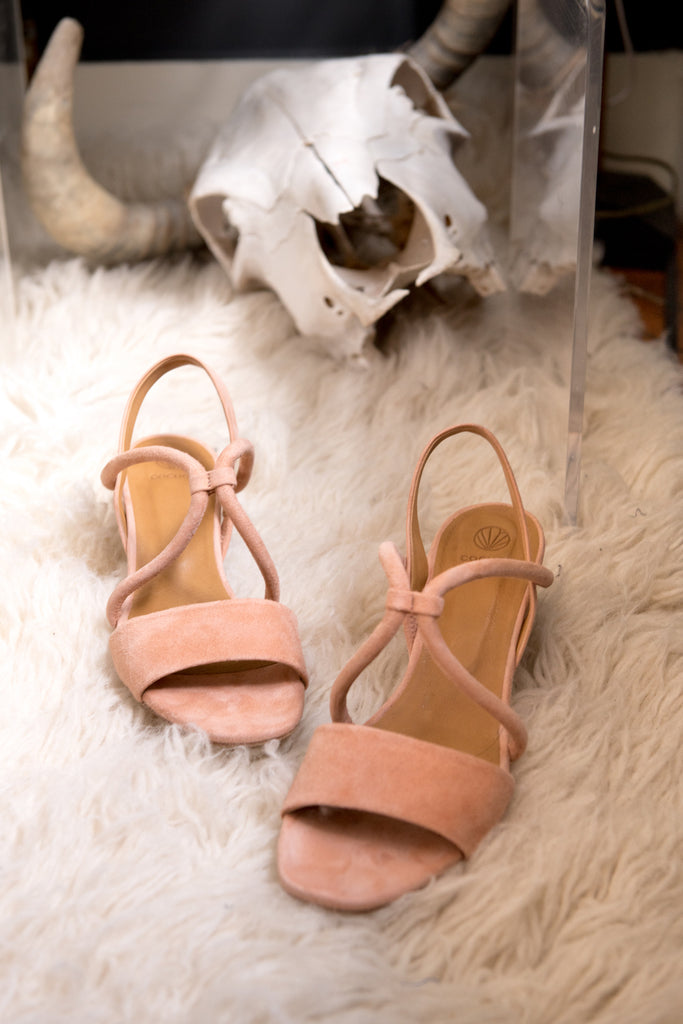 The Oasis Sandal in Depeche Suede displayed on a sheepskin rug with decor in background.