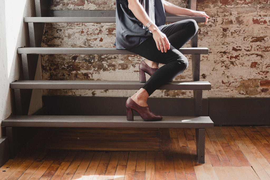 Below-shoulder image of sitting on a staircase sporting the Chenoa Heel in Chianti Leather.