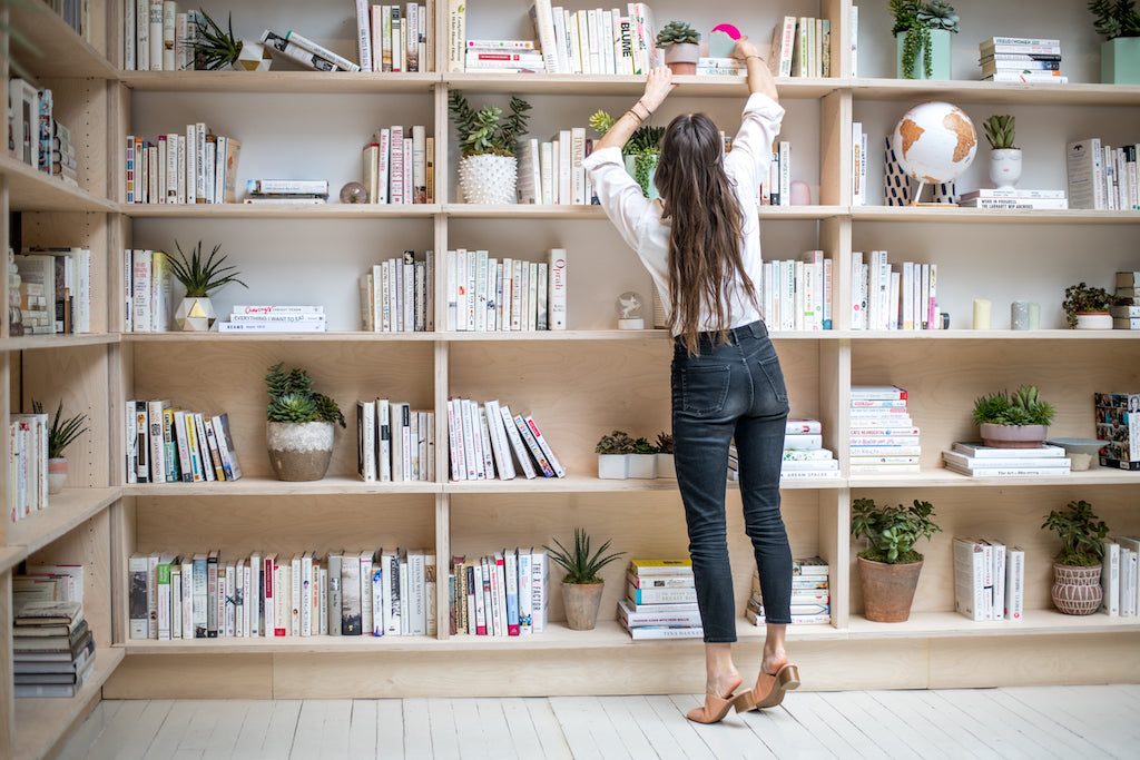 Image of Lolita Cros reaching up for a book on a bookshelf in her Coclico heels. 