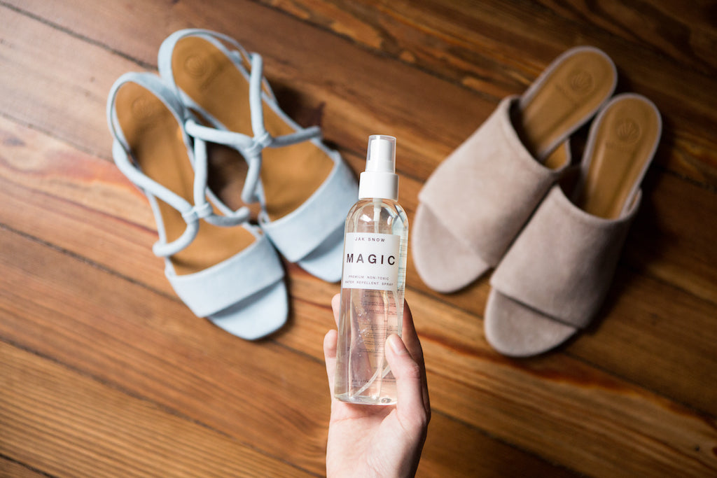 Woman holding the Jak Snow Magic Spray with two pairs of Coclico sandals on wood flooring. 