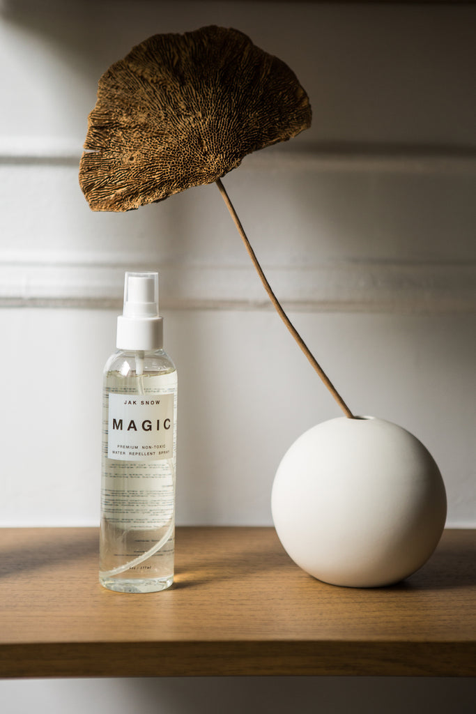 Close up image of the Jak Snow Magic Spray with a dried plant in a circular vase placed on the other side.  