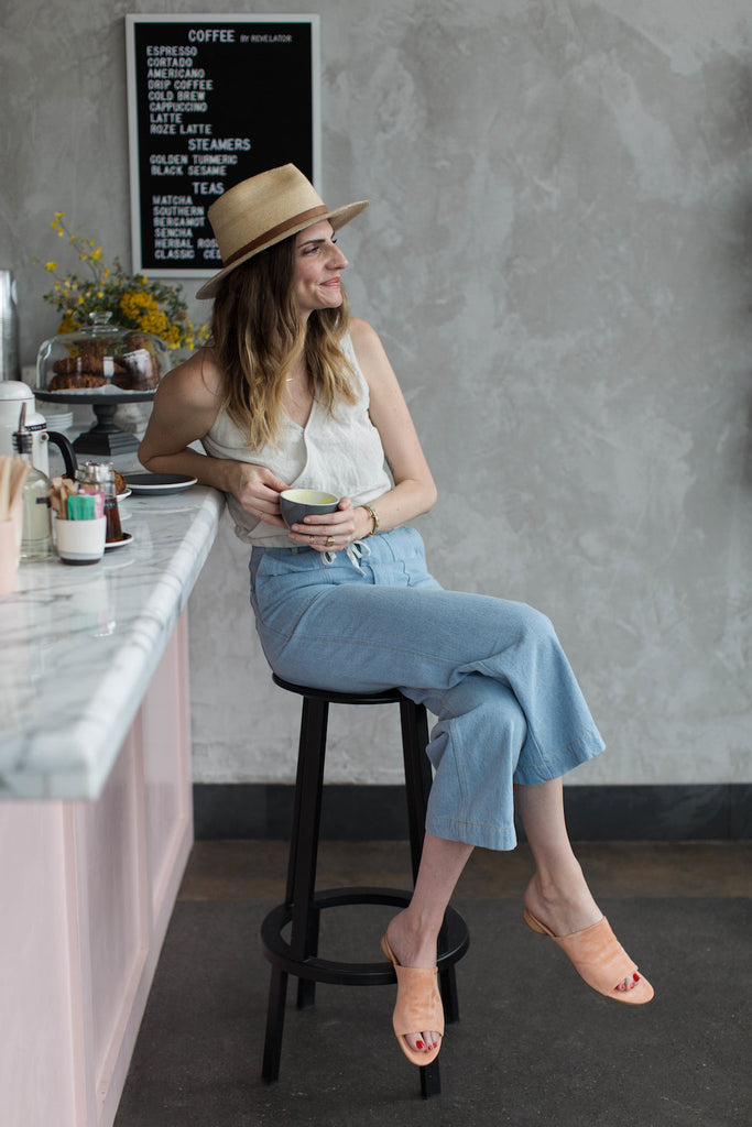 Ruthie Lindsey in Cafe Roze seated on a bar stool with a cup of coffee in hand.