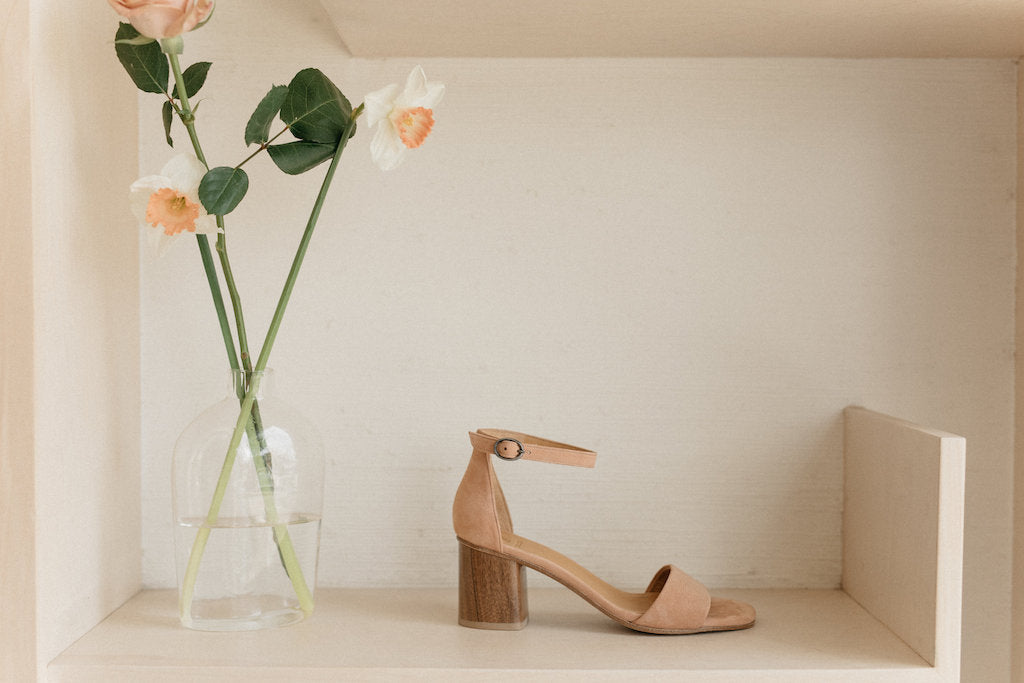 Side view of a Coclico Heel on display alongside a glass vase with a flower in it.   