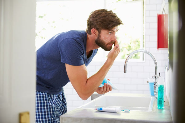 Man In Pajamas Putting On Moisturiser In Bathroom