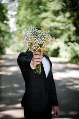 Groom holding flowers that are covering his face having made a fashion mistake at his wedding