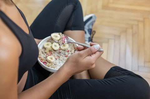 A girl in a crossed leg sitting position holding a bowl of oats with banana toppings