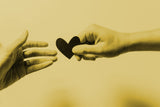 Hand giving a paper heart to another to showcase support