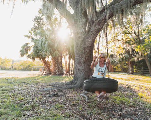 Woman on tire swing in Fuse Lenses tank top smiling with sun flare in background