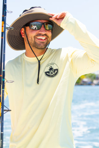 Man smiling with a yellow long sleeve Fuse Lenses shirt and a hat. He is holding a fishing pole and wearing grey polarized sunglasses.