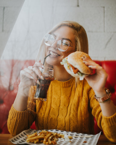 Women sitting while holding a burger and sipping on some coke. Photo by Angelos Michalopoulos on Unsplash