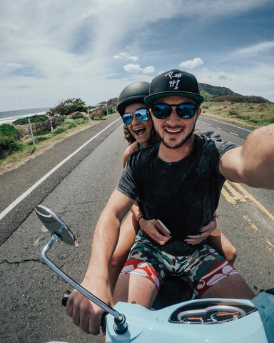 Couple wearing sunglasses riding moped together on scenic road