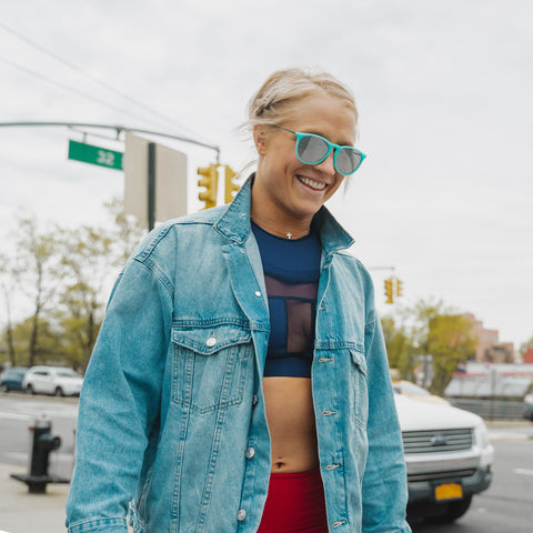 Blonde smiling woman wearing blue sunglasses walking down a street in New York City