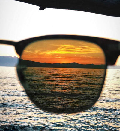 the view of a sunset on the water being looked at through tinted sunglasses
