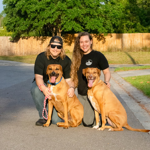 Fuse Lenses employees Jessica and Zach kneeling with dogs outdoors at golden hour in a cul-de-sac