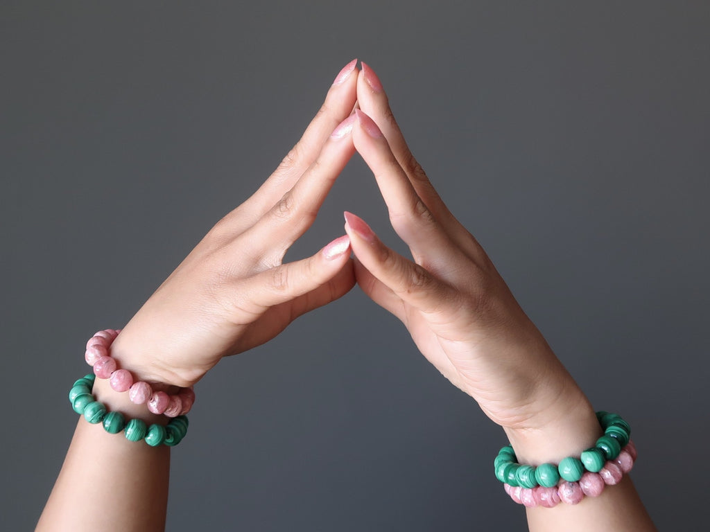 hands wearing malachite and rhodochrosite bracelet sets at satin crystals boutique