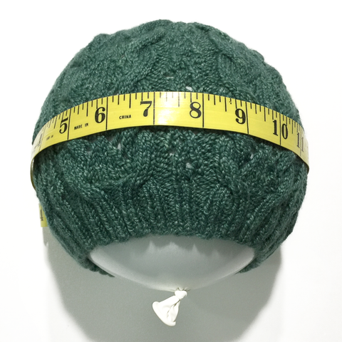 Green knitted hat pulled over a round balloon with measuring tape around the circumference