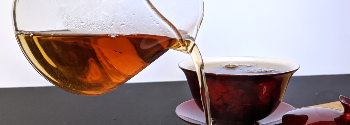 our bug bitten Eastern Beauty black tea is poured from a glass server with red gaiwan in background