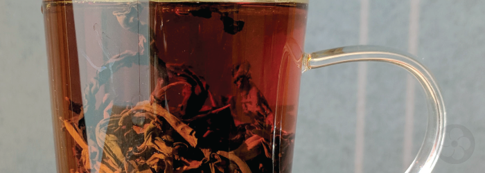 Whole black tea leaves steeping in a glass infuser mug