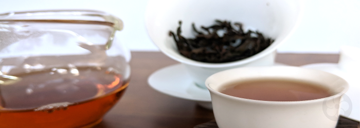 Da Hong Pao leaves in the background produce an amber brew in a glass server and tasting cup
