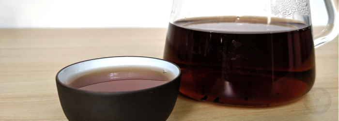 The dark color of aged pu-erh tea shows clearly in a glass server and tasting cup