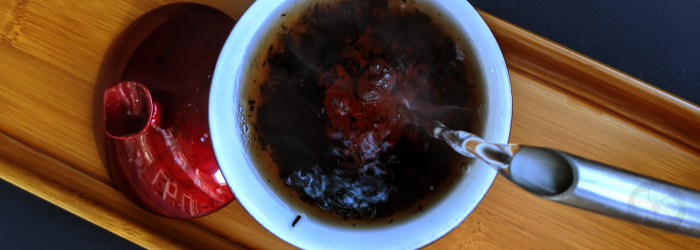 water is poured over pu-erh leaves in a gaiwan, producing a dark infusion