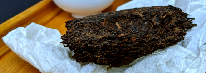 broken pu-erh cake with paper wrapper displays layers of compressed leaves