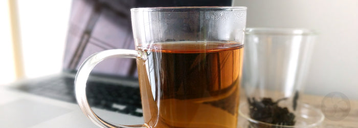 A glass infuser mug in front of a laptop computer, where it often joins us during work hours