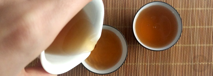 roasted tea is poured from a serving pitcher into two tasting cups on a bamboo mat