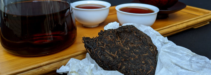 A pu-erh tea cake in front of brewed pu-erh tea shows the dark color of leaves and liquor.